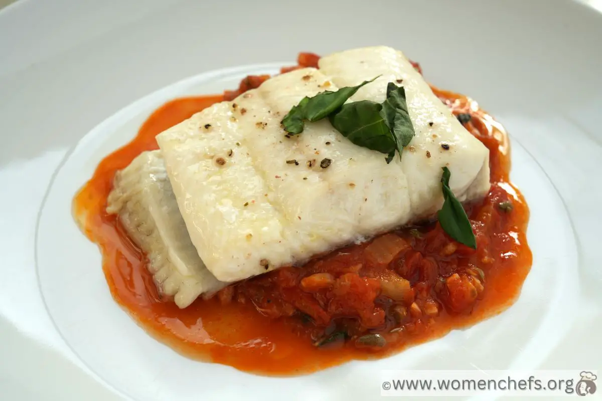 a portion of Ina Garten's baked halibut with tomato and caper sauce on a white plate