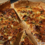 A baked Ina Garten quiche cut into slices on a wooden board